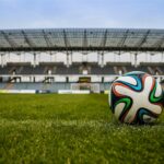 Close-up of a soccer ball on a lush grass field with an empty stadium in the background.